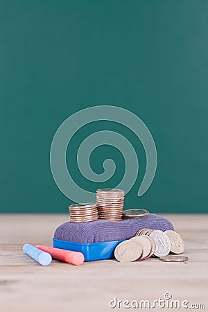 A blackboard eraser, a pile of dollar coins and two pieces of chalk in front of the blackboard background Stock Photo