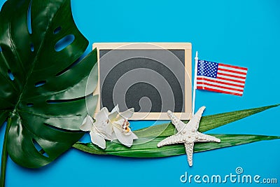 Blackboard and palm leaf with starfish, US flag. Stock Photo