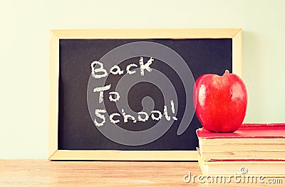 Blackboard with the phrase back to school, apple and stack of books. filtered image Stock Photo