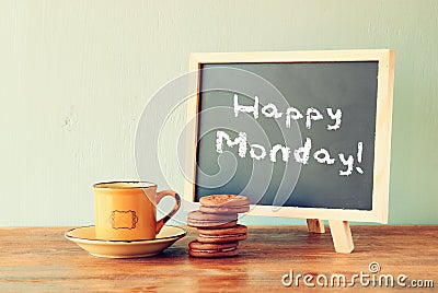 Blackboard with the phrase happy monday next to cup of coffee and cookies Stock Photo