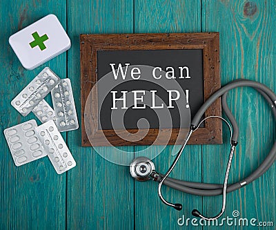 Blackboard with text & x22;We can help!& x22;, pills and stethoscope on blue wooden background Stock Photo