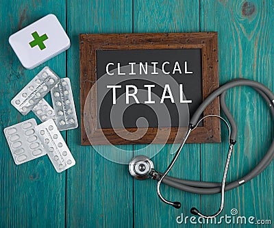 Blackboard with text & x22;Clinical trial& x22;, pills and stethoscope on blue wooden background Stock Photo