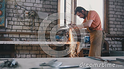 Blacksmith in forge - sharpening iron tools with sparkles - metal workshop Stock Photo
