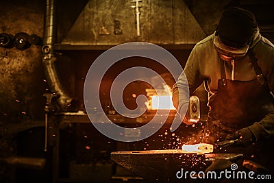 The blacksmith forging the molten metal on the anvil in smithy Stock Photo