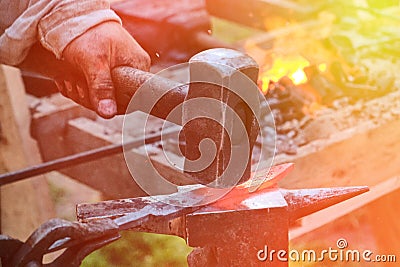 Blacksmith hammer hits the hot metal. Forging of iron objects in a retro forge. The process of working on the manufacture of Stock Photo