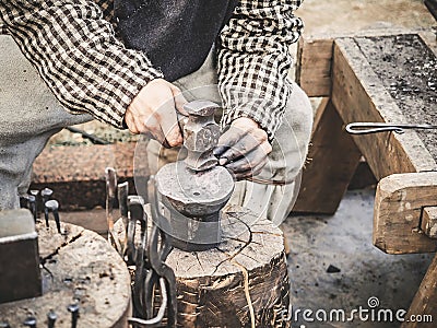 Blacksmith hand with a hammer on steel anvil . Hand of a blacksmith with hammer close up. The blacksmith in the Stock Photo