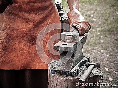 . Blacksmith hand with a hammer on steel anvil . Hand of a blacksmith in leather gloves with hammer close up. The Stock Photo