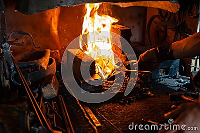 blacksmith holds billet over hot coals in clay oven. blacksmith heating iron metal sword manufacturing marching forge, Stock Photo