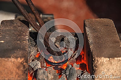 The blacksmith holds the tongs and heats the iron billet while the iron hotly creates a horseshoe on the anvil Stock Photo