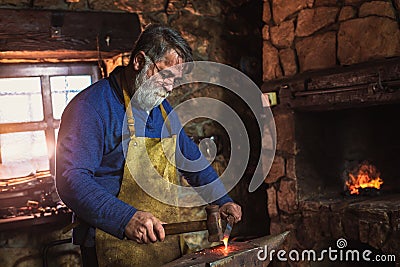 Blacksmith manually forging the molten metal on the anvil in smithy Stock Photo