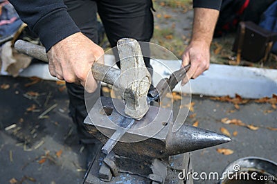 Blacksmiths hands holding forceps and a hammer forging a metal billet, blade of a knife, on an anvil Stock Photo