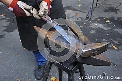 Blacksmiths hands holding forceps and a hammer forging a metal billet, blade of a knife, on an anvil Stock Photo