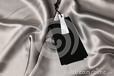 Blank black tags on silver silky fabric. Space for text Stock Photo