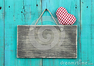 Blank distressed wood sign with red checkered heart hanging on rustic antique teal blue door Stock Photo