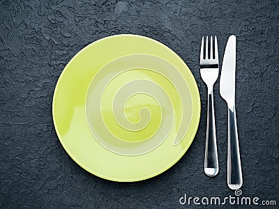 Blank flat yellow plate, fork on dark gray stone concrete table, top view. Mock up, copy space Stock Photo