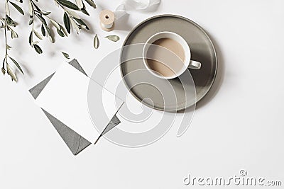 Blank greeting card, envelope mock-up. Cup of coffee, olive tree branches and silk ribbon isolated on white table Stock Photo