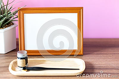 Blank landscape wooden frame beside a small houseplant and calligraphy tools, painting or artwork display mockup Stock Photo