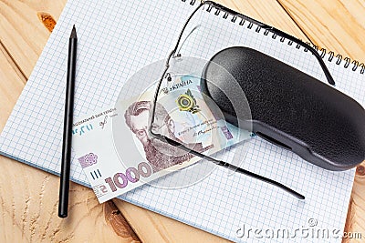 Blank notebook, glasses and ukrainian money on a wooden background. Banknote of 1000 hryvnia. Hryvnia UAH.. Close-up Stock Photo