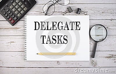 Blank notebook with text DELEGATE TASKS on the white background with calculator and office tools Stock Photo