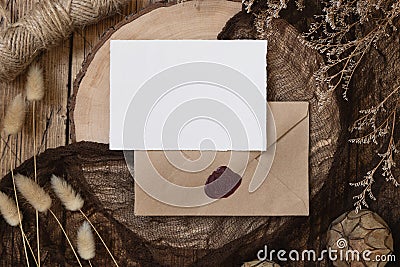 Blank paper card on sealed envelope and wooden table with dried plants Stock Photo