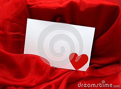 Blank paper note card with red heart on red silk fabric background. Stock Photo