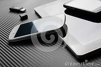Blank Phones With Reflection Lying And Leaning On Business Tablet Beside An USB Flash Drive Above A Carbon Background Stock Photo