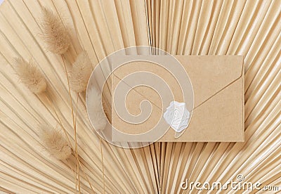 Blank sealed envelope on dry beige palm leaf near hare`s tail grass top view, boho wedding mockup Stock Photo