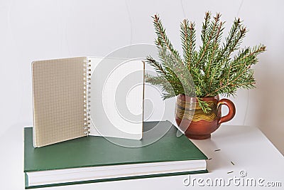 Blank sheets of opened notepad on green book, bouquet of christmas tree branches in clay mugn Stock Photo