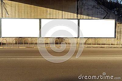 Blank street billboards on a grunge concrete wall in an underpass. Metal bollards, sidewalk and asphalt road in front. Stock Photo