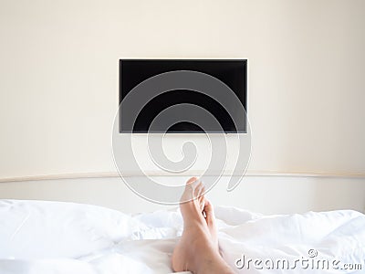 Blank television on white wall in front of the bed. first person view from bed seeing men feet and TV. Stock Photo