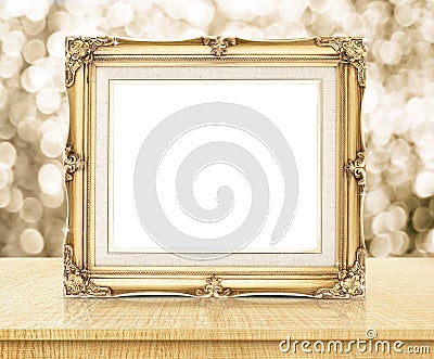 Blank victorian style golden frame with sparkling gold bokeh wall and wooden table, business concept presentation. Stock Photo