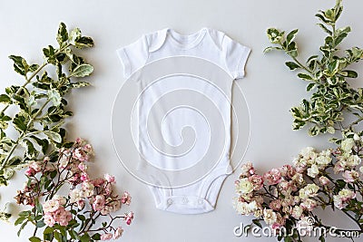 Blank White Baby Grow On An Off White Background With Green Leaves and Pink Roses Stock Photo