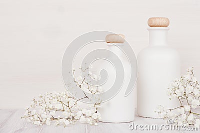 Blank white cosmetics bottles with small flowers on white wood board, mock up. Stock Photo