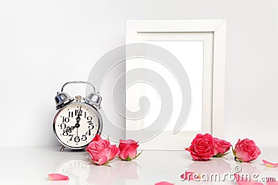 Blank white frame, pink roses and alarm clock. Mock up. Stock Photo