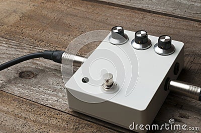 A blank white guitar pedal with vintage knobs and plugged jacks on the floor Stock Photo