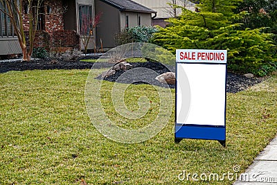 Blank white lawn sign in the grass in front of a house. A sign on top says Sale Pending. Stock Photo