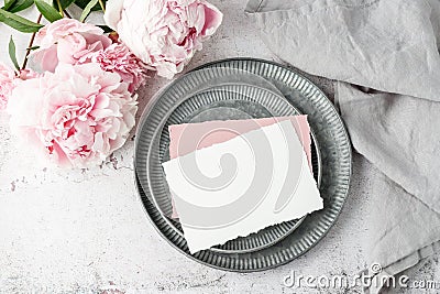 Blank white and pink paper postcard, on retro metallic tray, peony flowers and grey linen napkin on grunge stone background Stock Photo