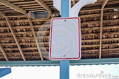 Blank white sign with red boarder attached to a blue post with the inside of the wooden ceiling as a background Stock Photo