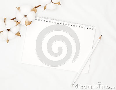 Blank white spiral notebook with pencil and cotton flowers on white bed sheet. Stock Photo