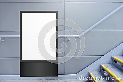 Blank white vertical digital display in front of painted concrete wall, beside flight of stairs. Template for mock up of Stock Photo