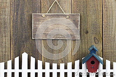 Blank wood sign hanging over white picket fence with birdhouse Stock Photo