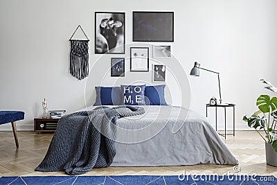 Blanket on bed with blue pillows in white bedroom interior with gallery and lamp on table. Real photo Stock Photo