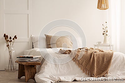 Blanket on white bed in natural bedroom interior with plants and wooden stool Stock Photo