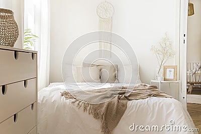 Blanket on white bed with pillows and wooden cabinet in minimal natural bedroom interior Stock Photo