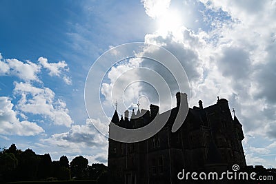 Dark silhouette scary looking medieval castle back-lit by sun behind passing clouds Stock Photo