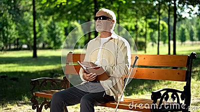 Blind pensioner reading braille book, sitting on bench in summer park, resting Stock Photo