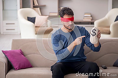 Young blindfolded man holding moneybag at home Stock Photo