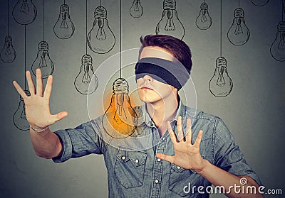 Blindfolded man walking through light bulbs searching for idea Stock Photo