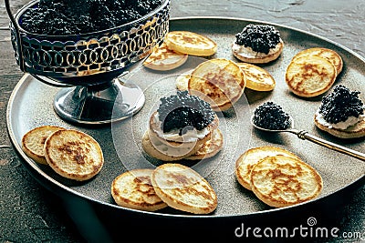 Blinis with black caviar, on a festive dish on a black background, mini pancakes Stock Photo