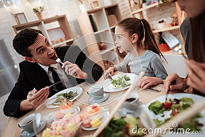 Blissful family eating dishes at table together. Parents with their daughter gathered at table. Stock Photo